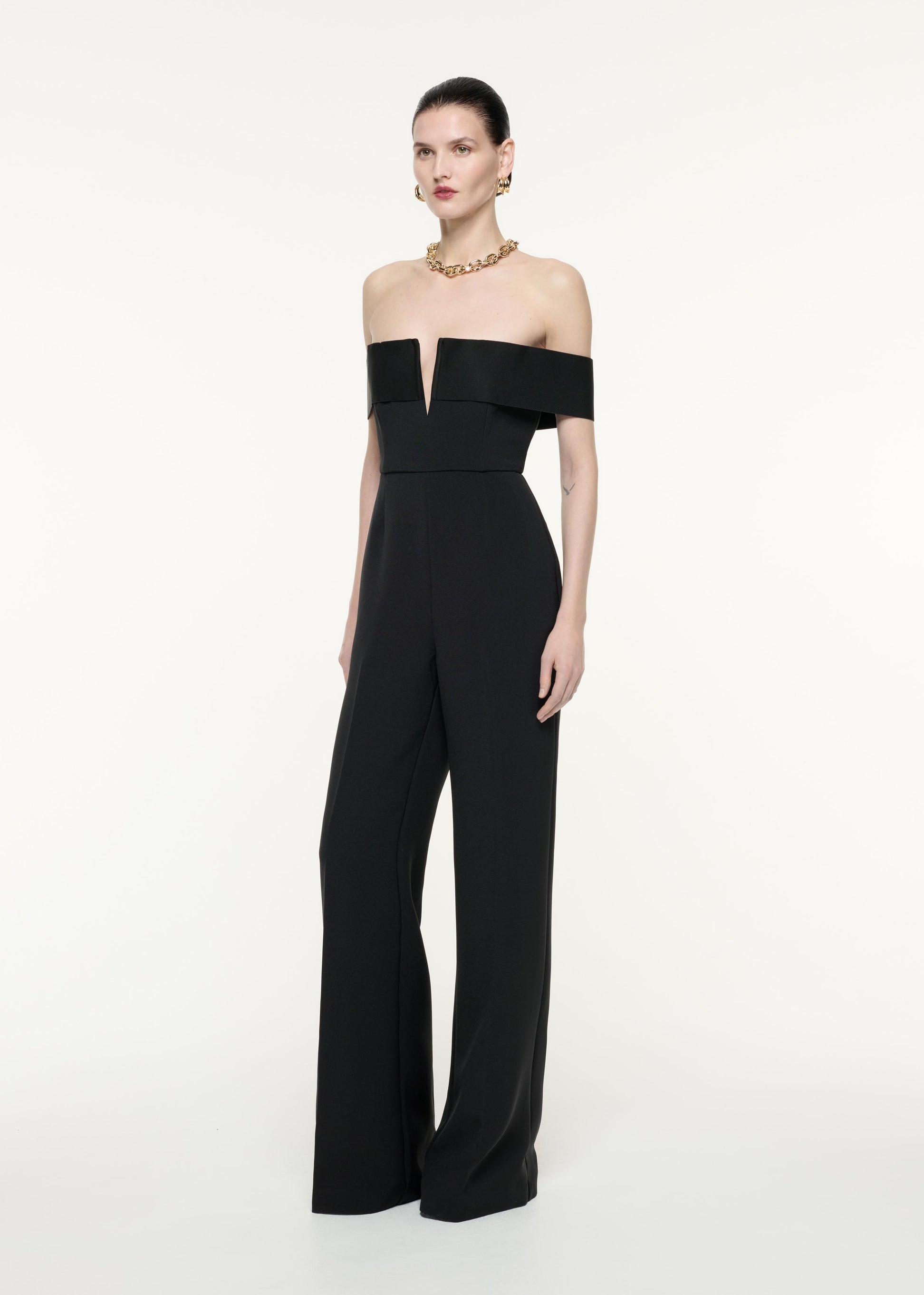 A side view image of a model wearing the Off The Shoulder Crepe Jumpsuit in Black