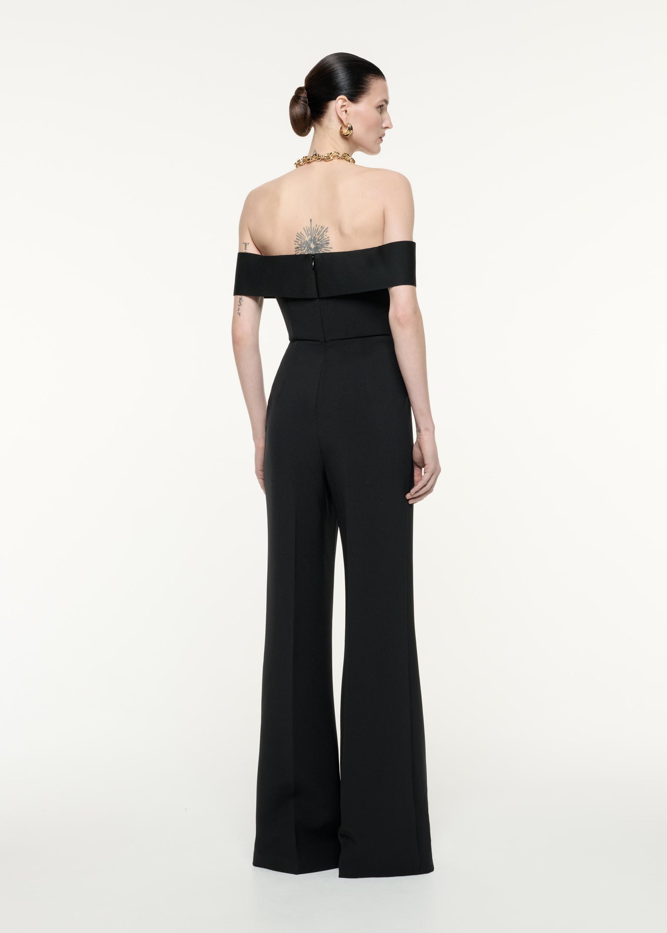 A back view image of a model wearing the Off The Shoulder Crepe Jumpsuit in Black