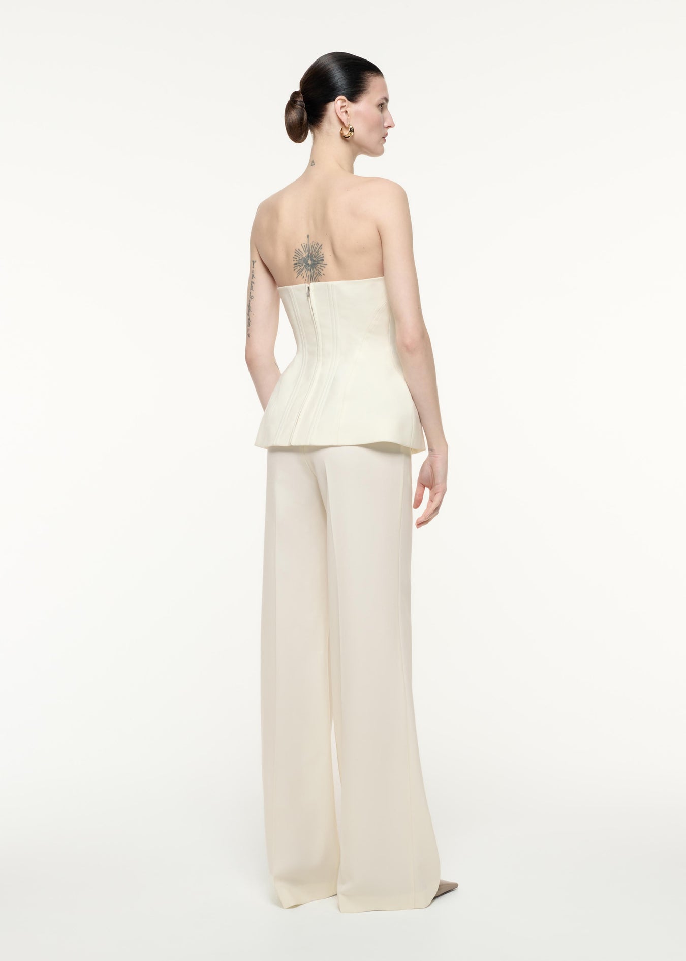 A back view image of a model wearing the Strapless Tailoring Wool Jumpsuit in Cream