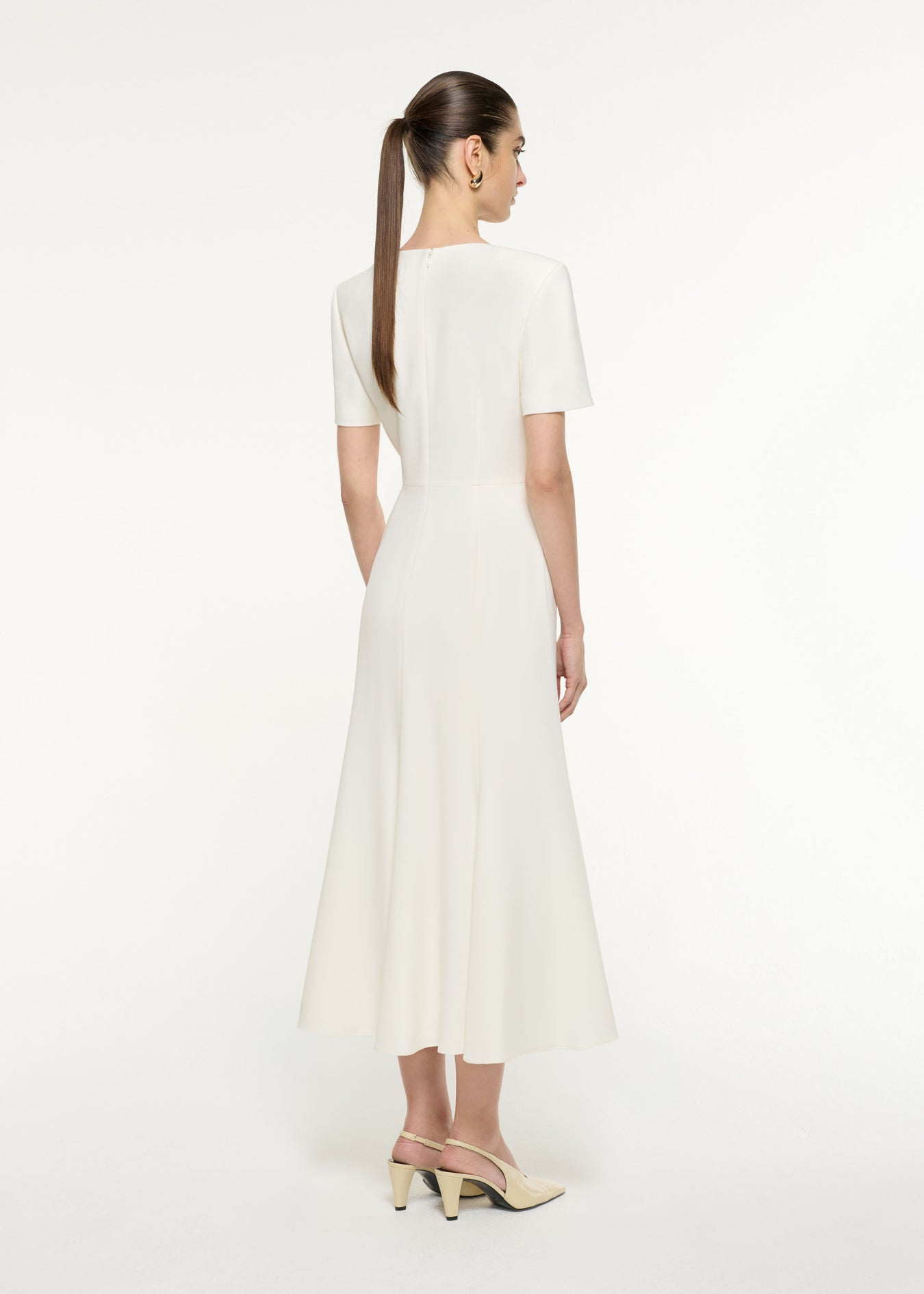 Back view of a model wearing the Bow Drape Light Cady Midi Dress in Cream