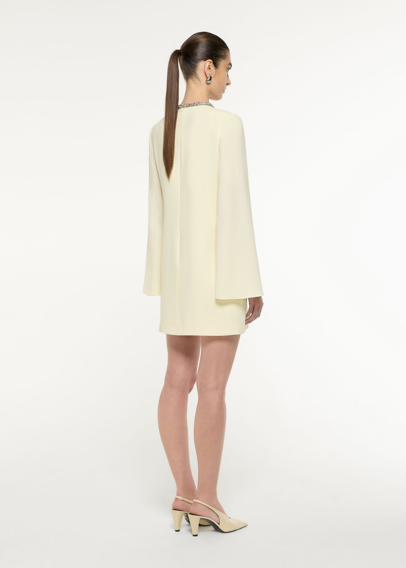 Back view of a model wearing the Cape Sleeve Embellished Mini Dress in Light Yellow